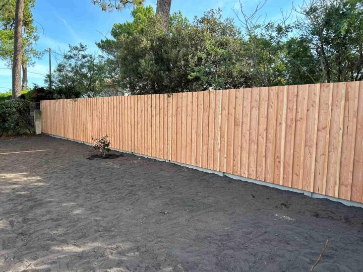 Réalisation d'une clôture en planches de bois verticales.
